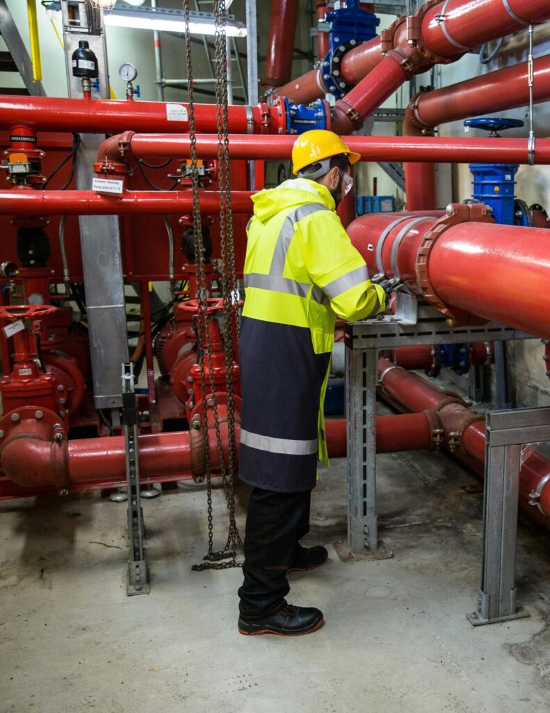 Engineer with safety gear inspecting red industrial piping system indoors.