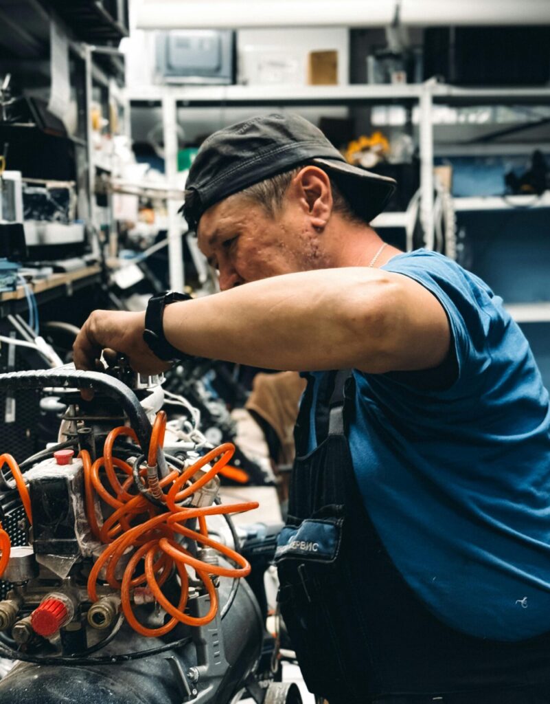 Skilled mechanic repairing air compressor in a cluttered workshop setting.
